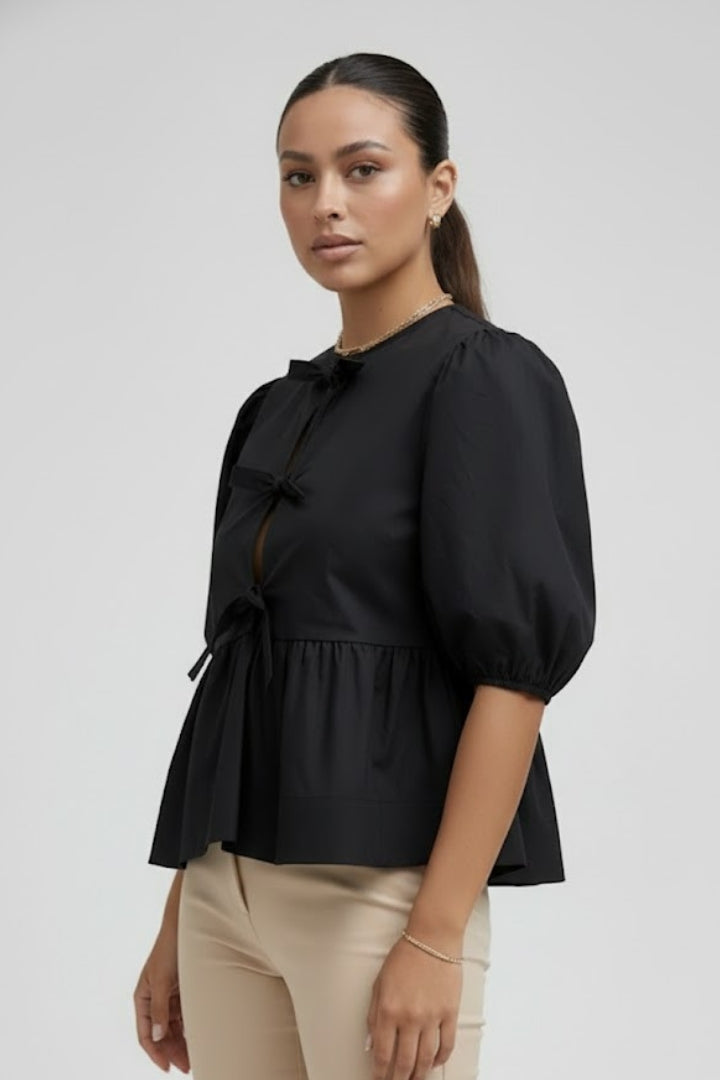 Women’s peplum blouse with bow details, button-down front, puffed sleeves, and flared hem for casual and occasion styling.
