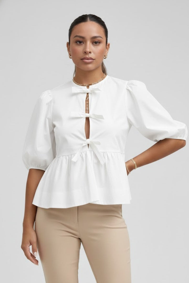 Women’s peplum blouse with bow details, button-down front, puffed sleeves, and flared hem for casual and occasion styling.