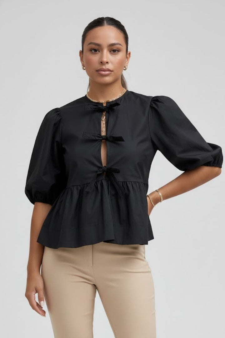Women’s peplum blouse with bow details, button-down front, puffed sleeves, and flared hem for casual and occasion styling.