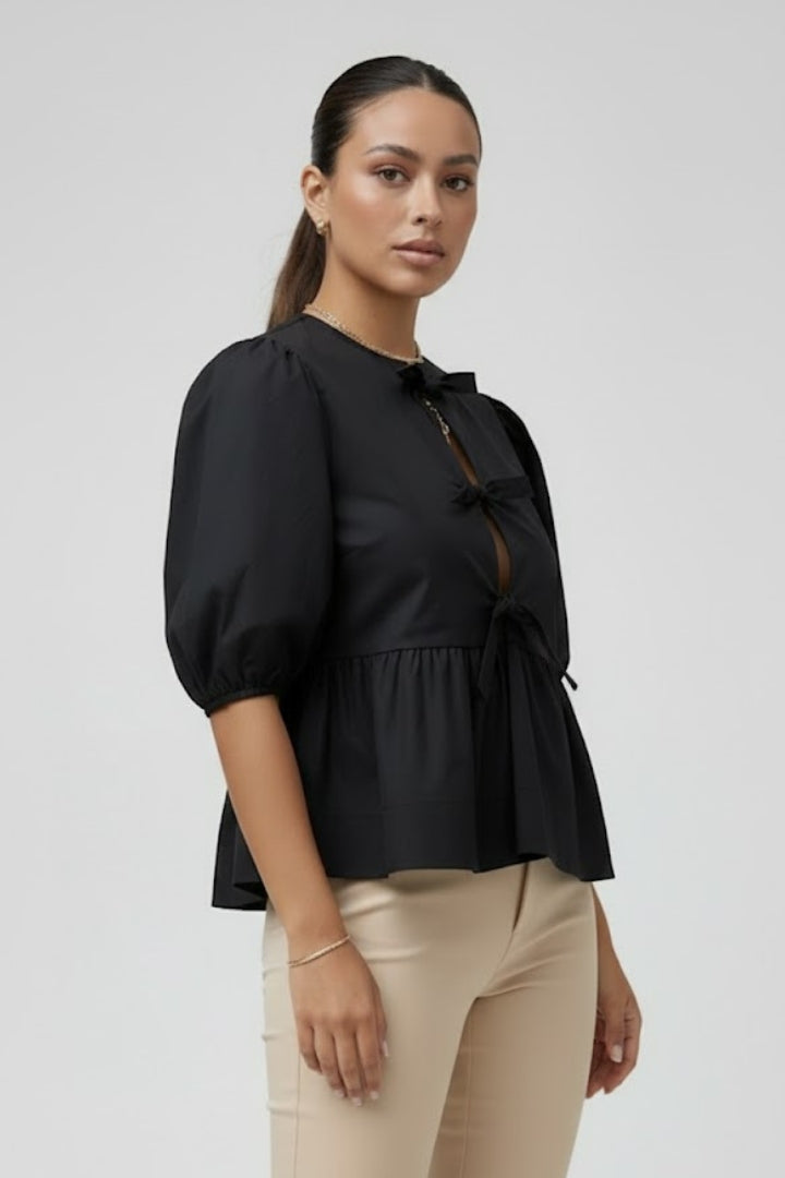 Women’s peplum blouse with bow details, button-down front, puffed sleeves, and flared hem for casual and occasion styling.